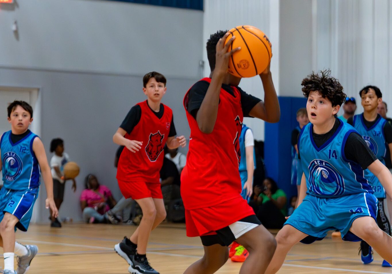 Young boys playing basketball indoors, one in red shooting.