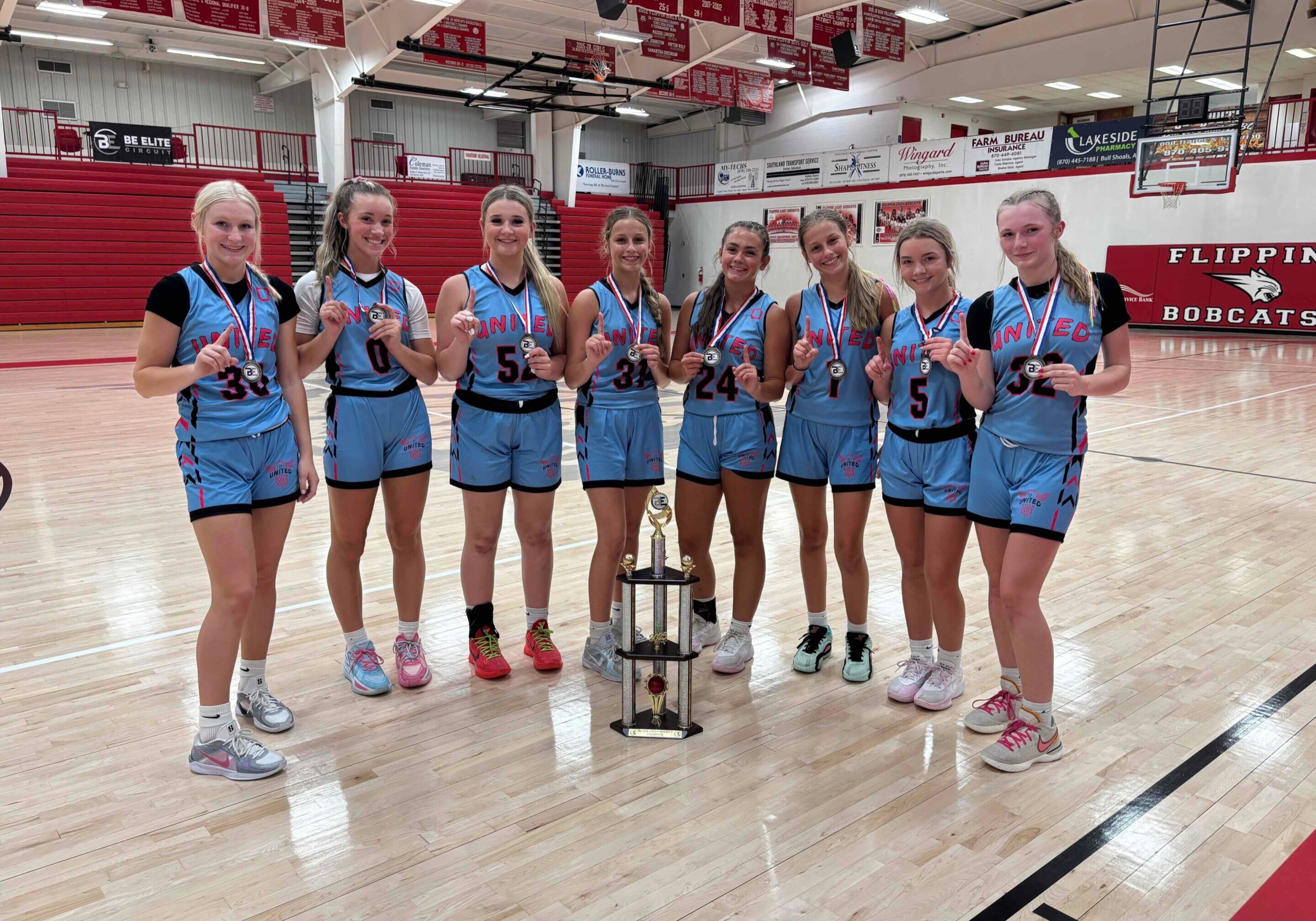 Girls' basketball team celebrating with trophy in gymnasium.